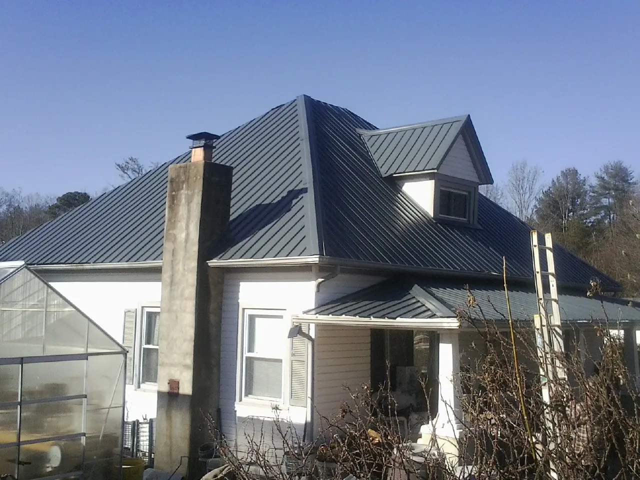 Dark blue standing seam metal roof on a white farmhouse with dormer — Slate & Tile Roof Repair by Roofing Brothers in Swainsboro