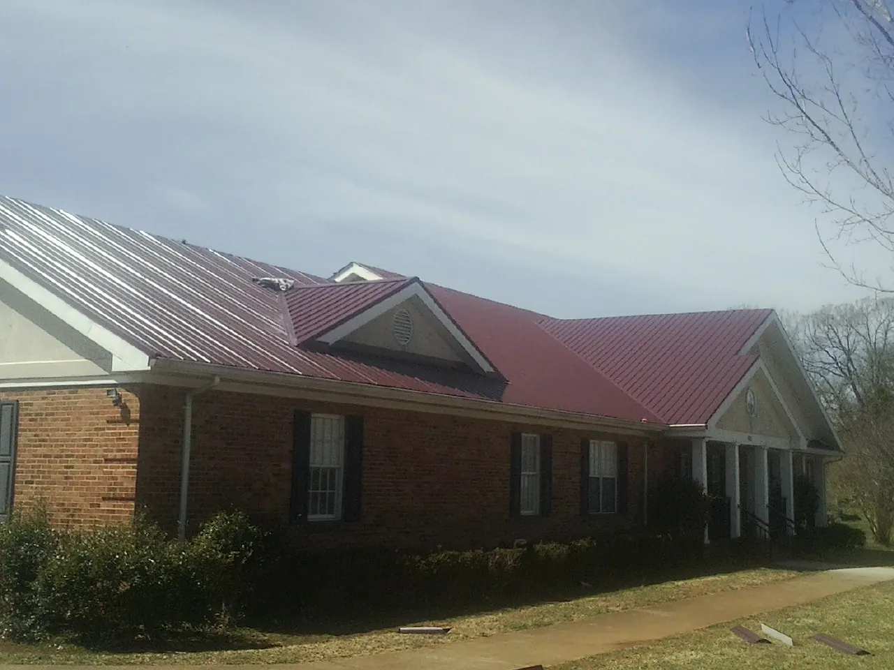 Red metal roof with gabled entries on a long brick building, from a Hail Damage Roof Repair job in Swainsboro
