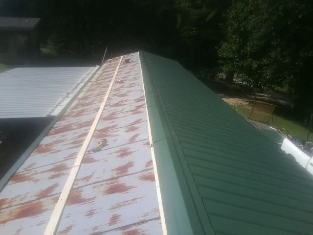 Old rusted panels beside newly installed green metal roofing — Wind Damage Roof Repair by Roofing Brothers in Swainsboro
