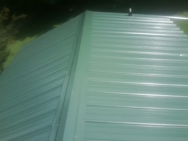 New green metal panels meeting at the ridge of a roof — Flat Roof Repair work by our crew in Swainsboro