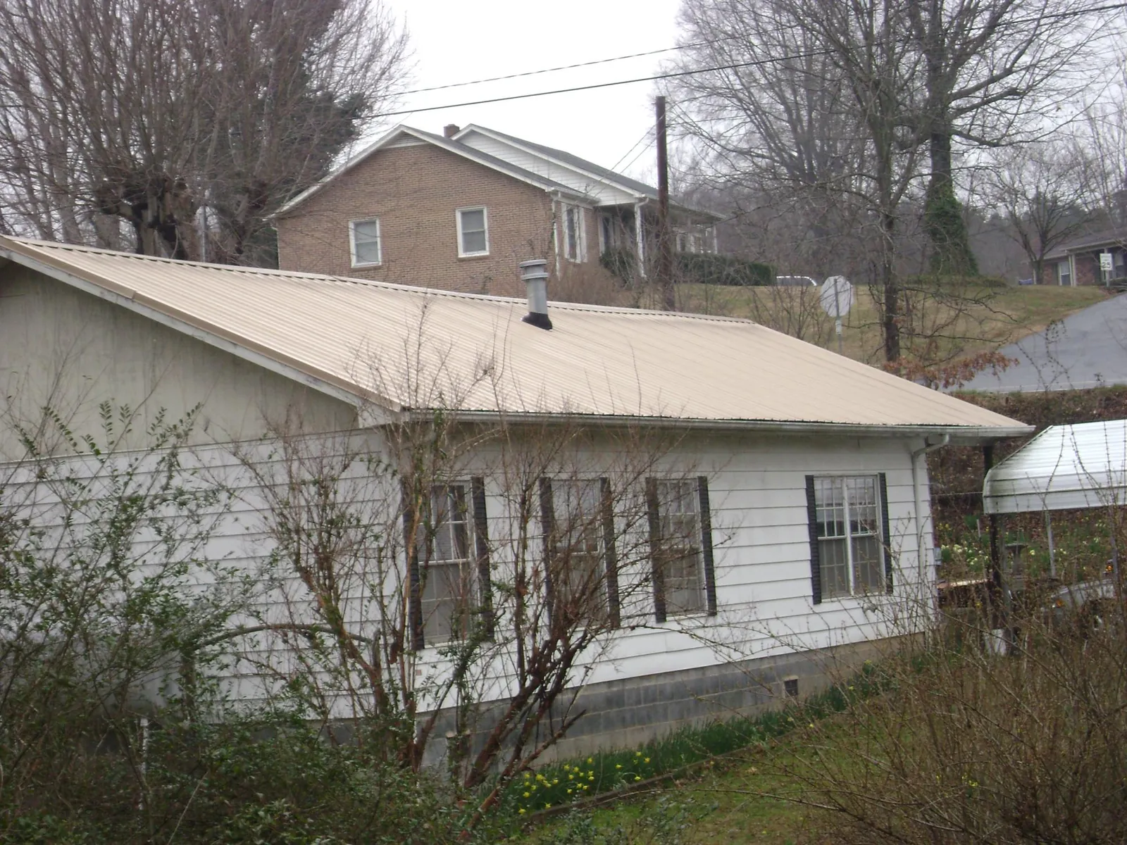 Tan metal roof on a white sided house set into a hillside — Commercial Roofing by Roofing Brothers in Swainsboro